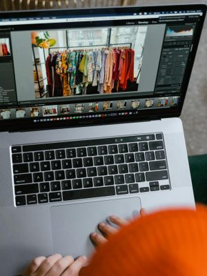 A person in a cozy setting edits photos of clothing displays on a laptop.