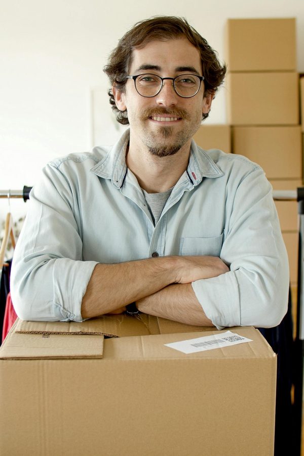 Smiling man with eyeglasses standing behind a cardboard box in a startup office setting.