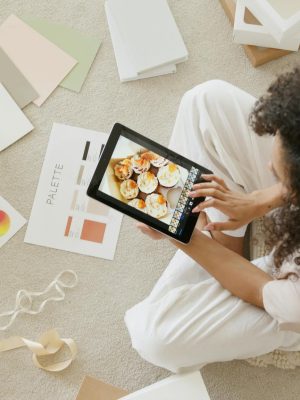 Woman using tablet surrounded by design tools and gift box, showcasing creativity and online work.